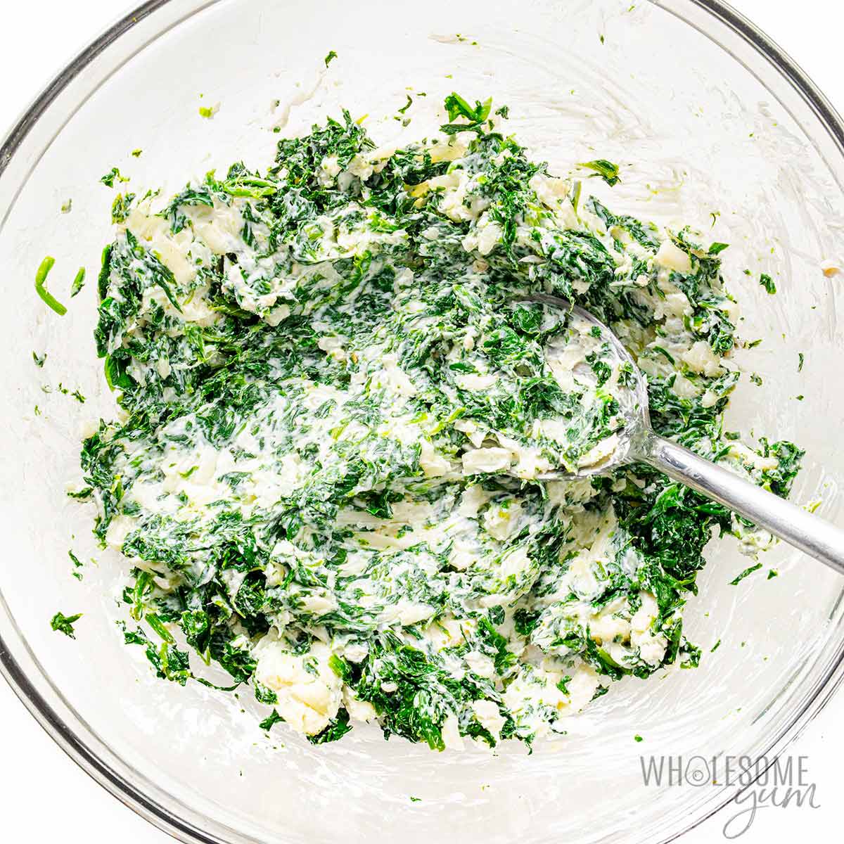 Spinach mixed into cheese mixture in a bowl.