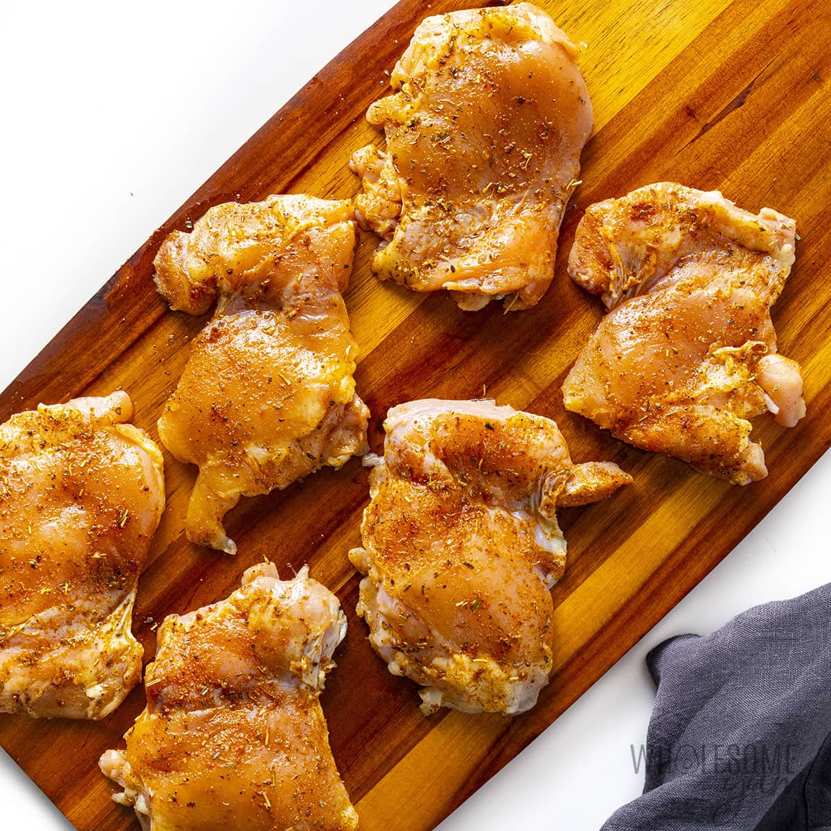 Raw boneless skinless chicken thighs seasoned on a cutting board.