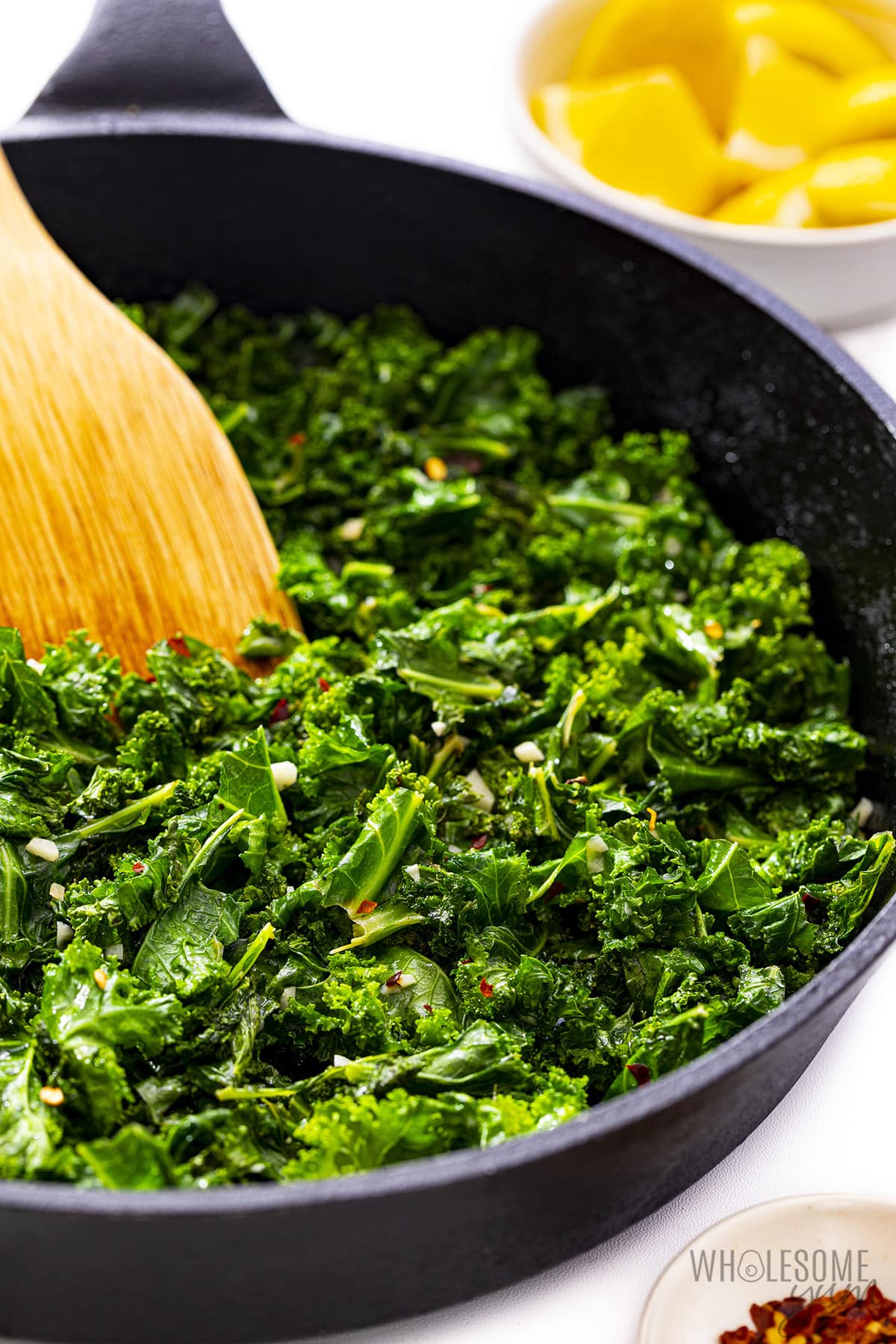 Sauteed kale in a skillet with wooden spoon.