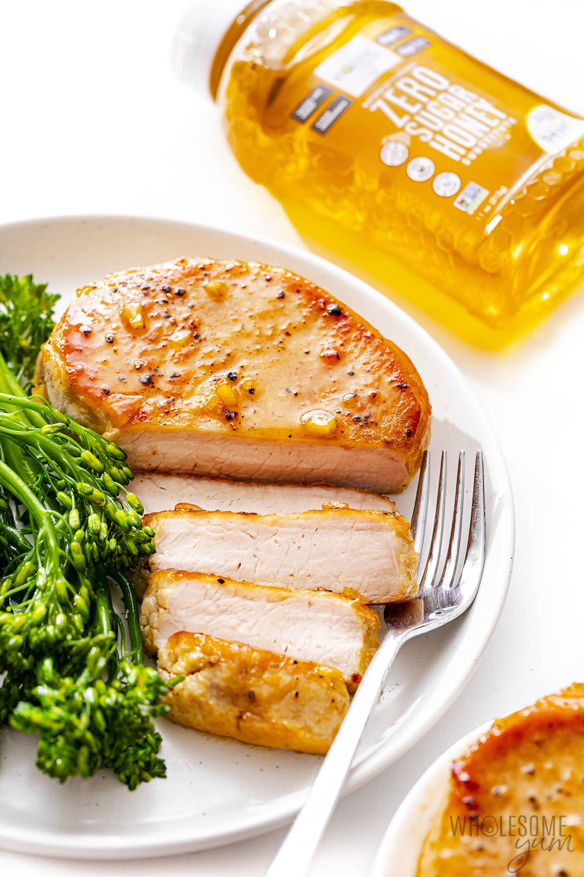 Keto pork chops on a plate with broccolini next to honey.