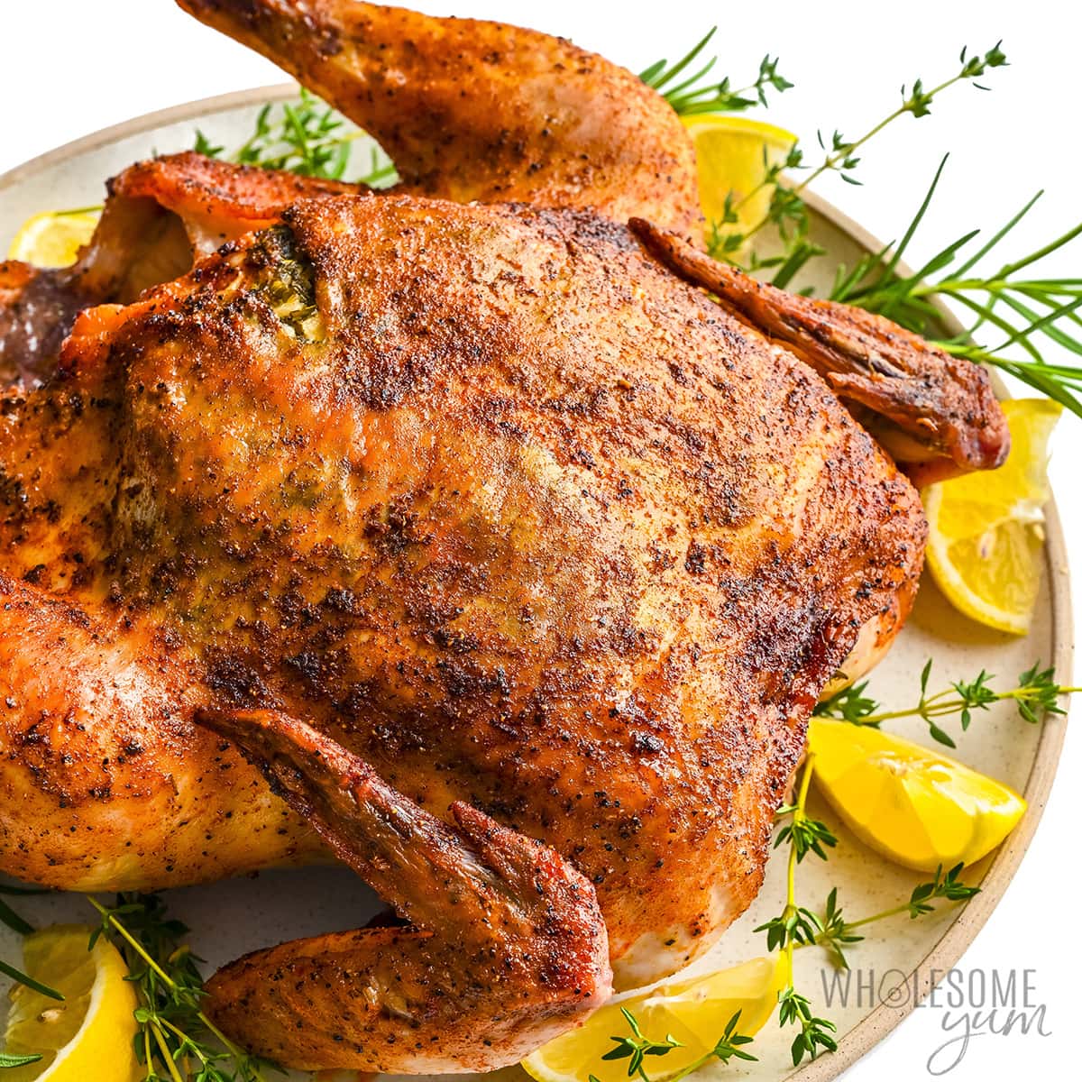 Roasted chicken on a platter with herbs and lemon wedges.