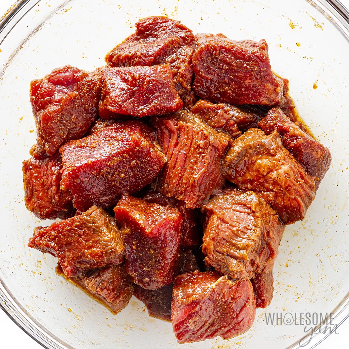 Steak pieces tossed in olive oil and seasonings in a bowl.