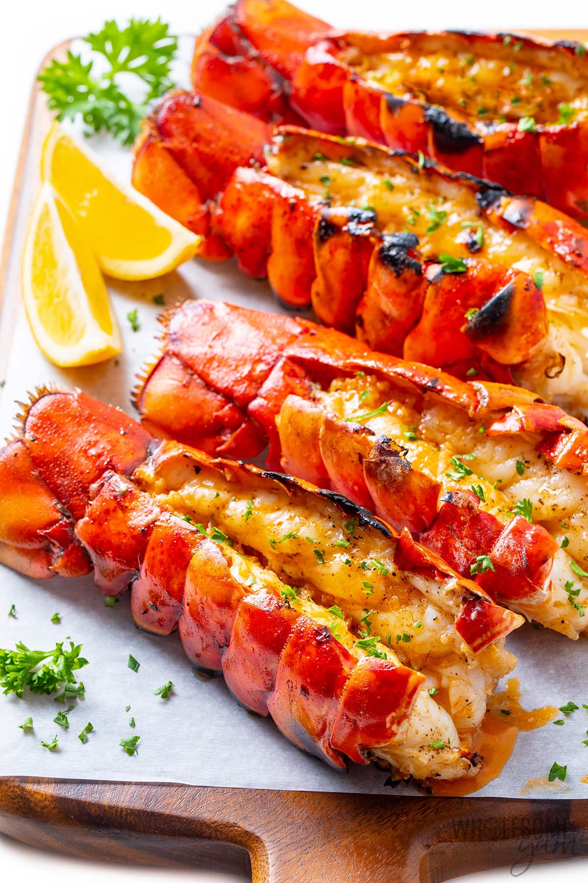 Four juicy grilled lobster tails on a cutting board and ready to serve.
