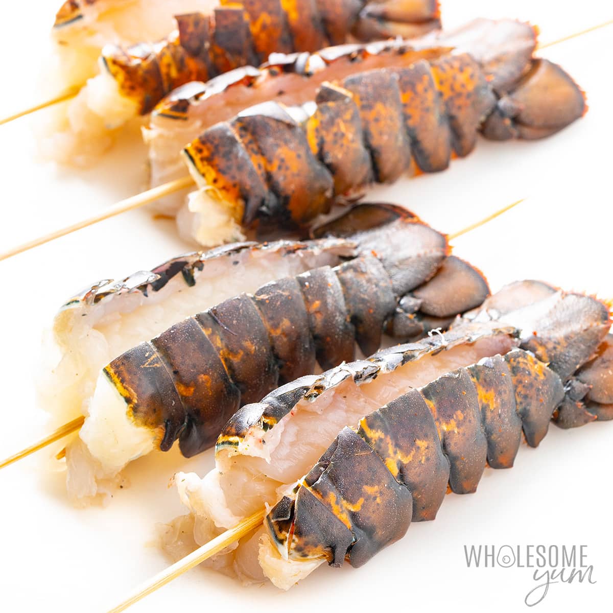 Butterflied lobster tails with wooden skewers through them.