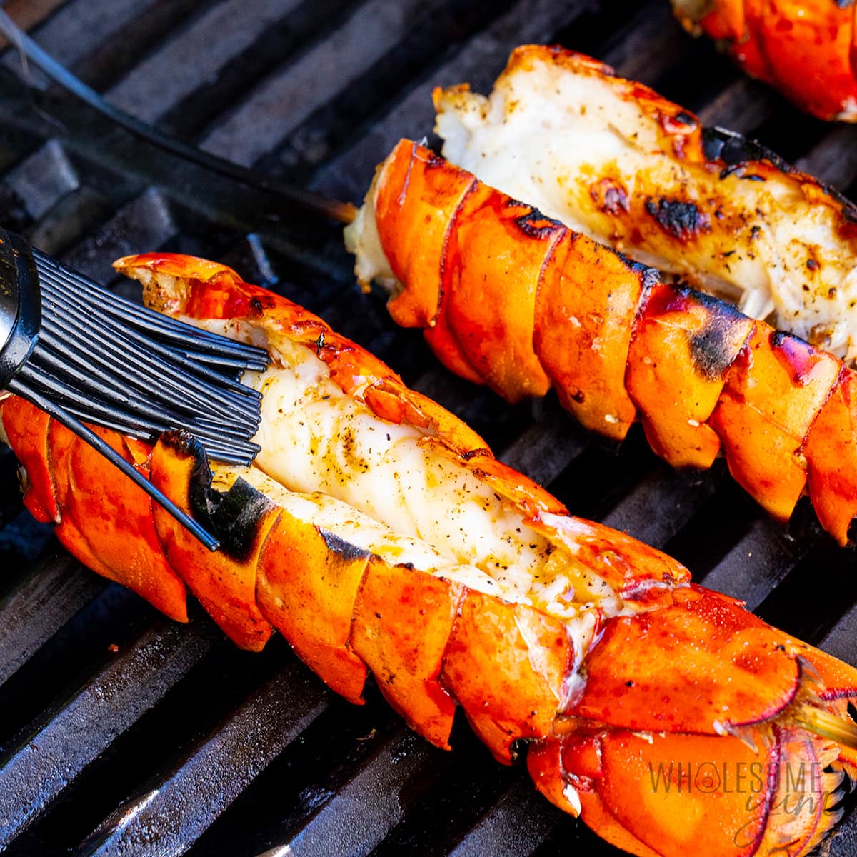 Brushing lobster tails on the grill with garlic butter.
