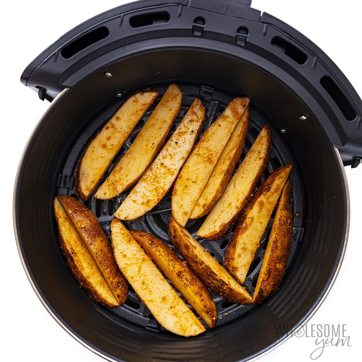 Seasoned potato wedges in an air fryer basket.