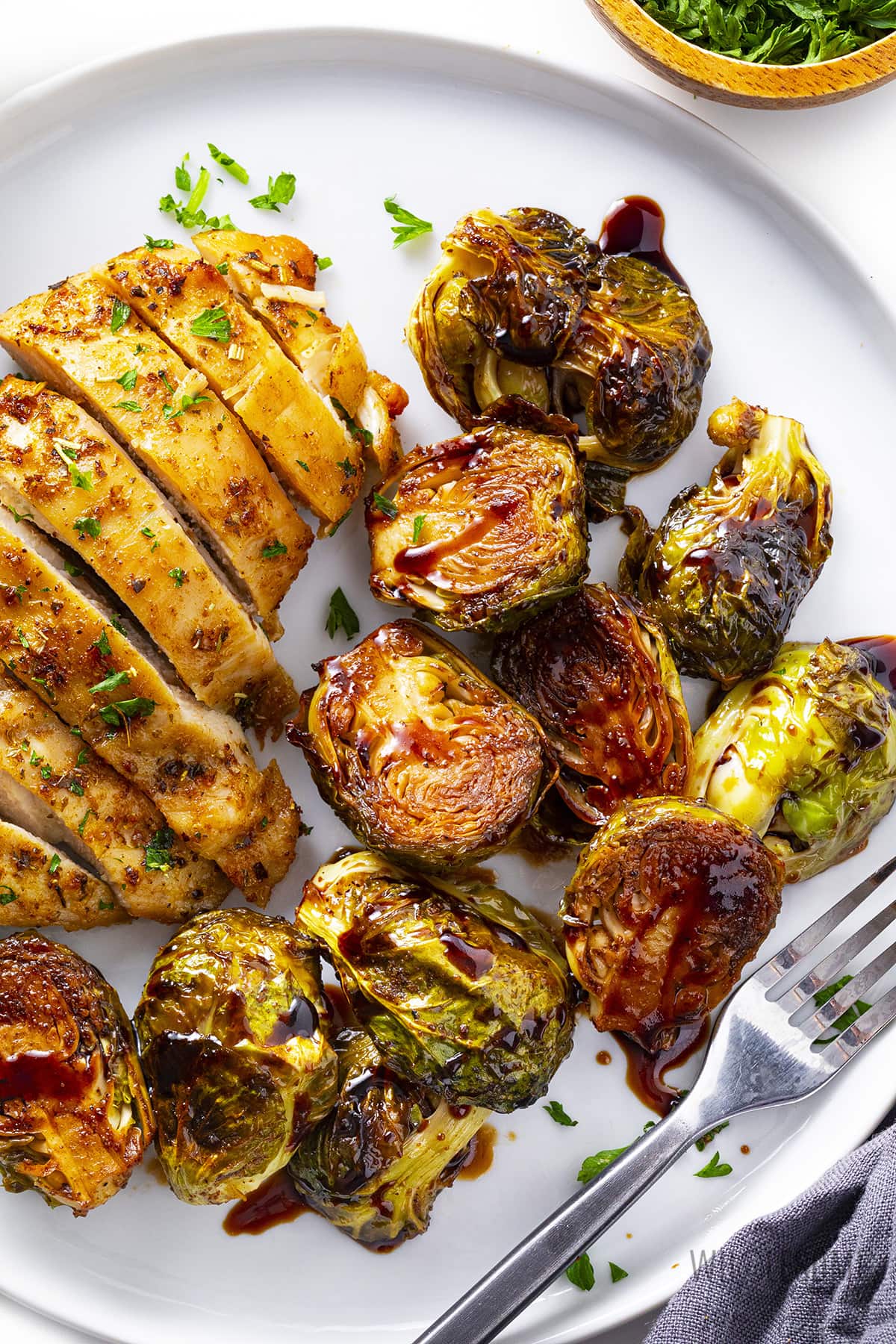 Balsamic glazed brussels sprouts on a plate with sliced chicken.