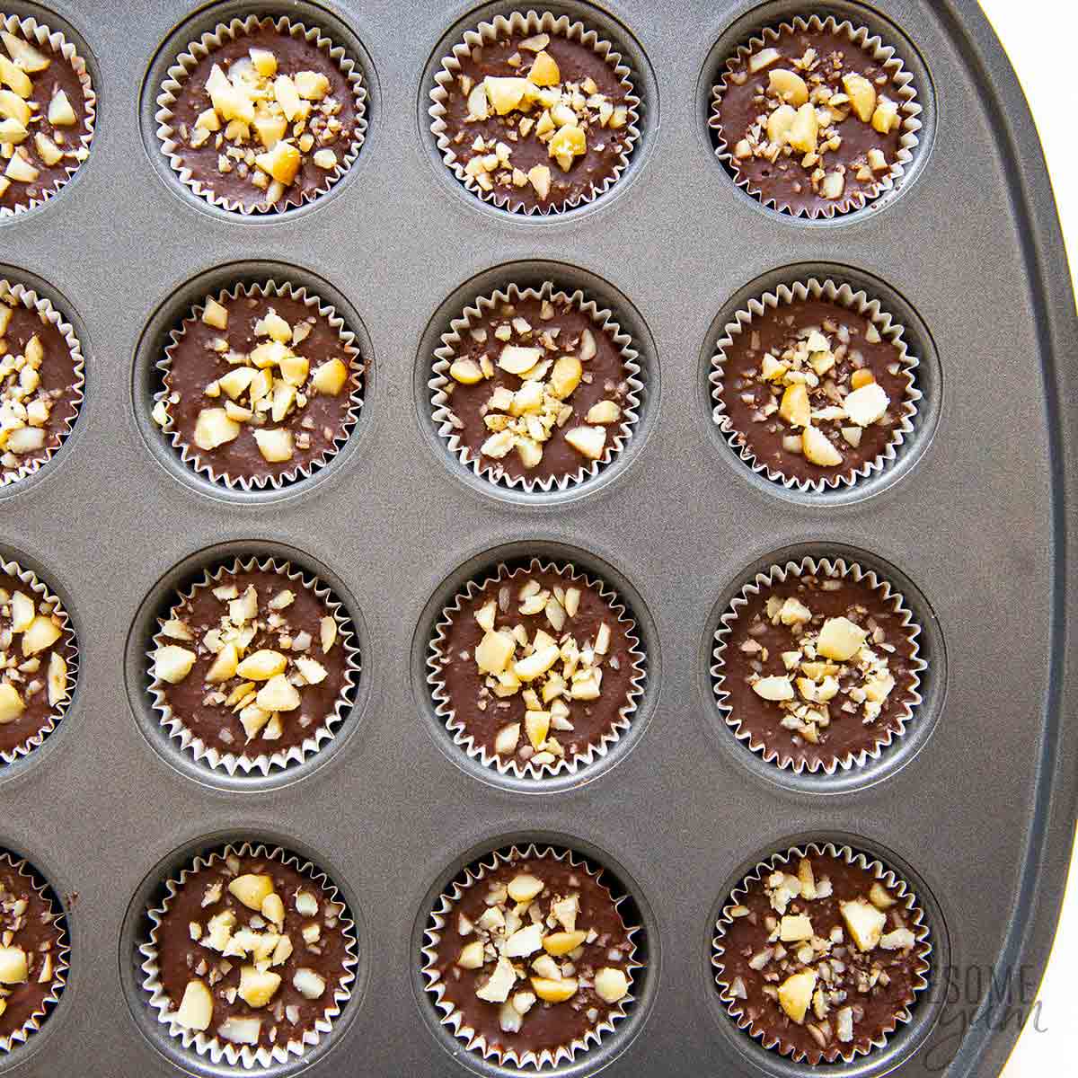 Keto fat bombs topped with nuts in a muffin tin.
