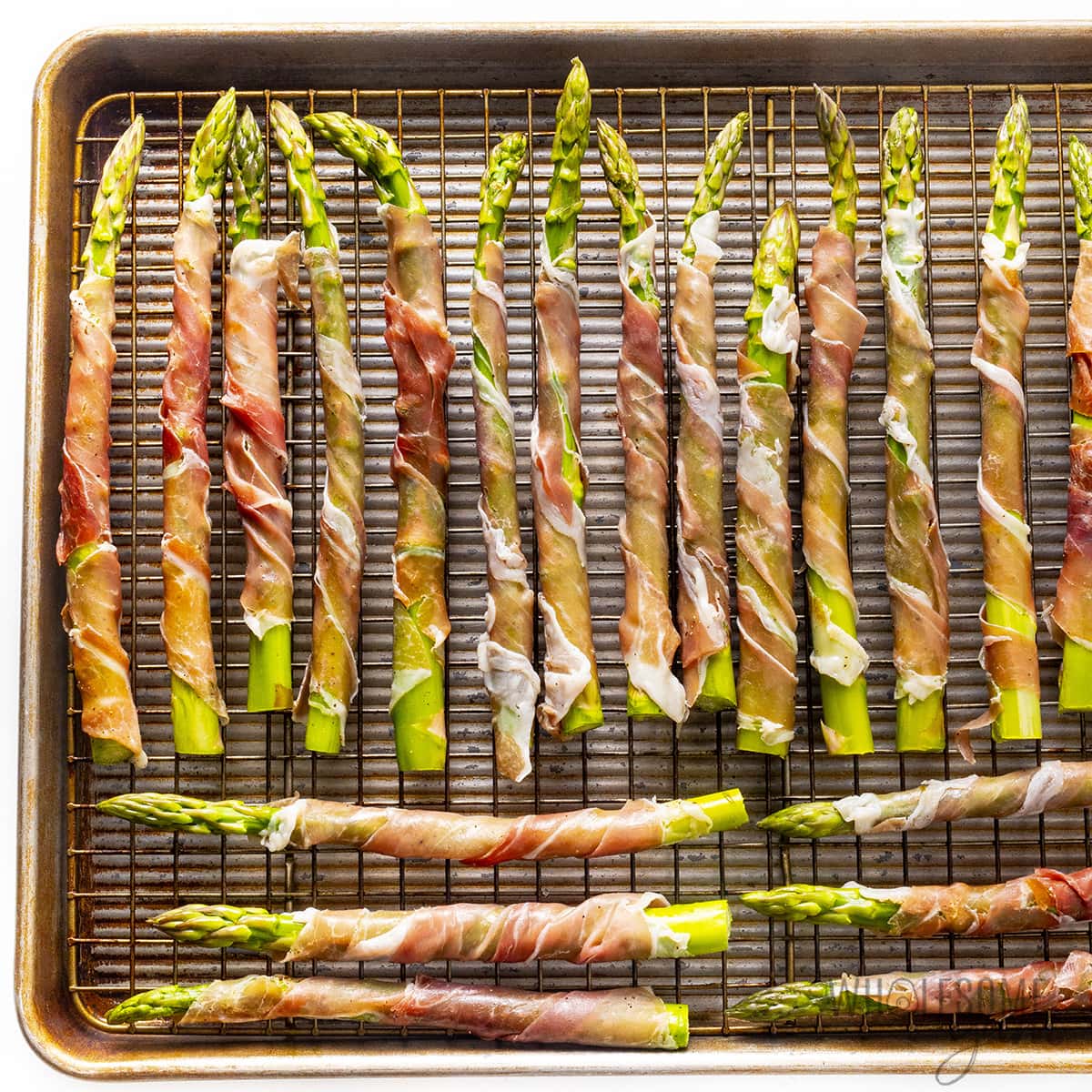 Asparagus wrapped with prosciutto on a baking sheet.