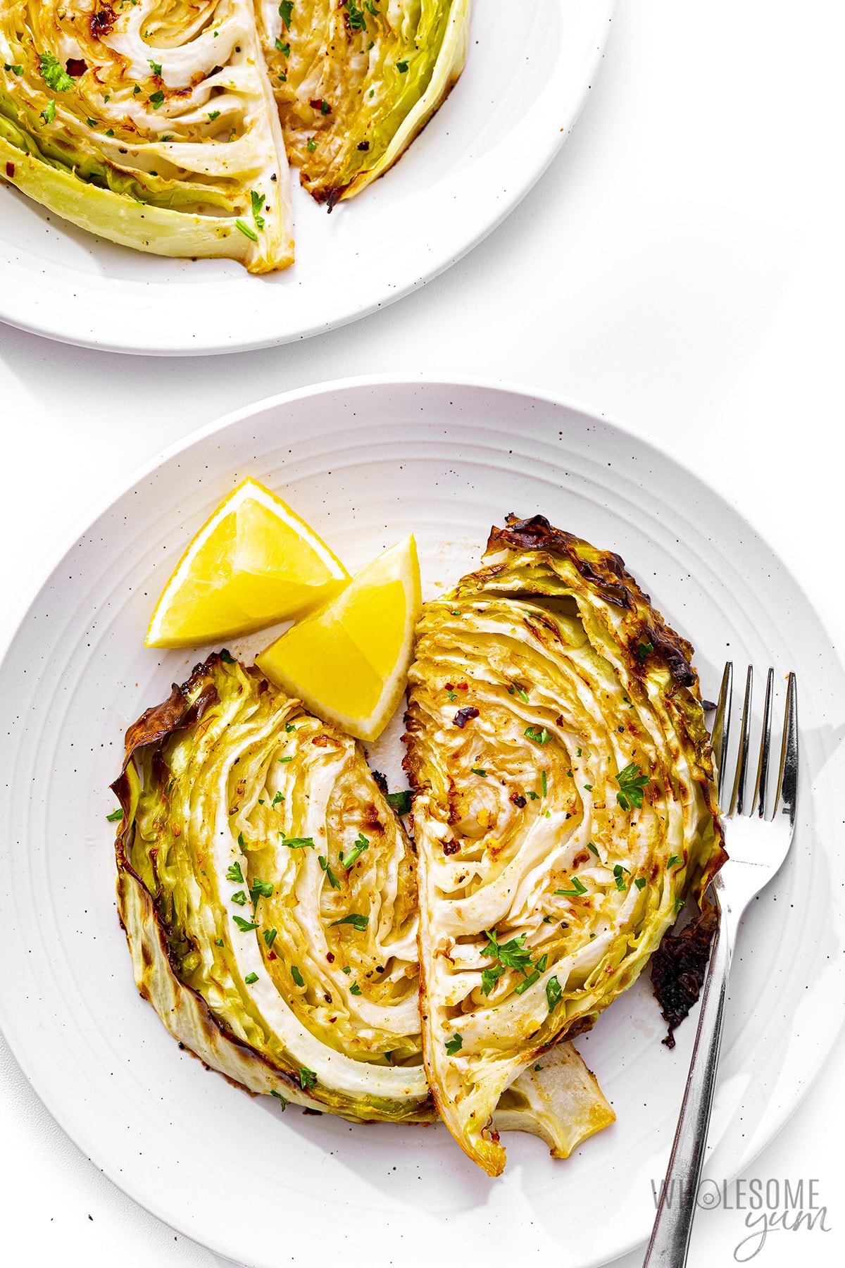 Roasted cabbage on a plate with a fork and lemon wedges.
