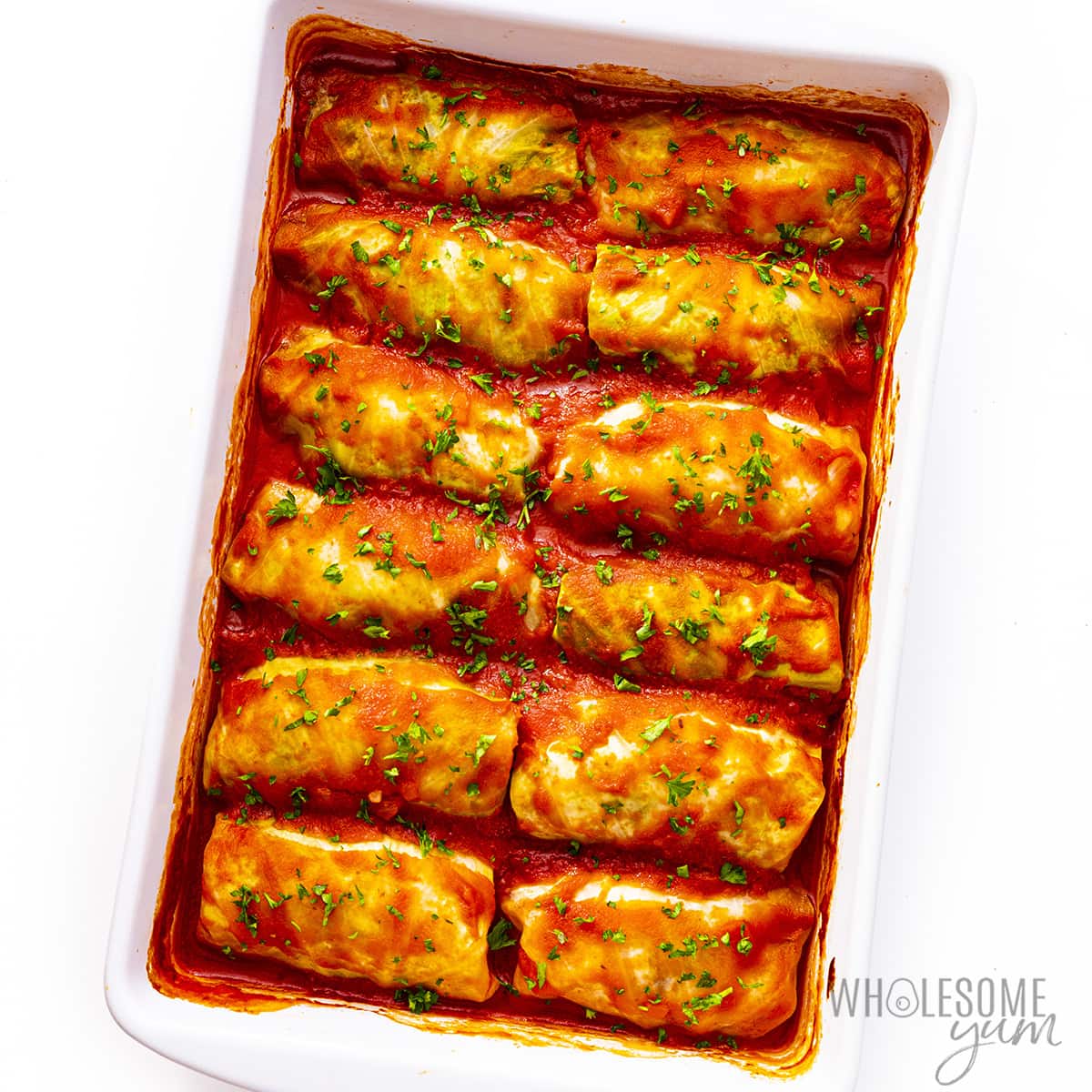 Baked stuffed cabbage rolls in a baking dish, with parsley for garnish.