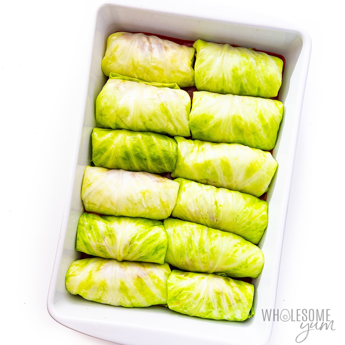 Cabbage rolls in a baking dish on top of sauce.
