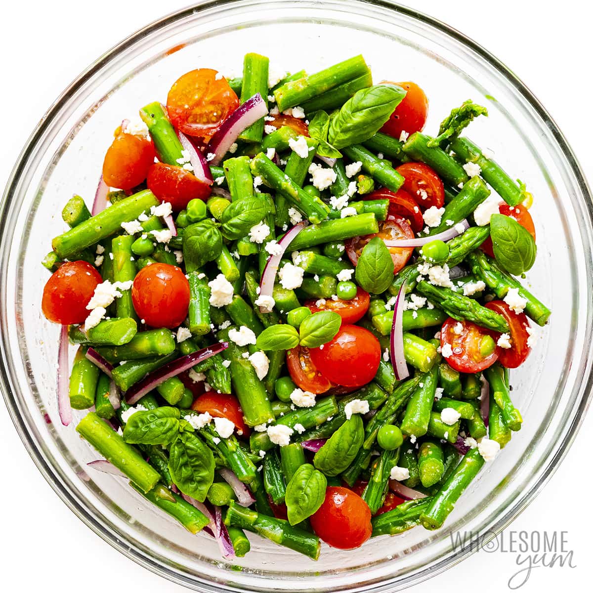 Tossed asparagus salad with feta cheese and basil leaves on top.