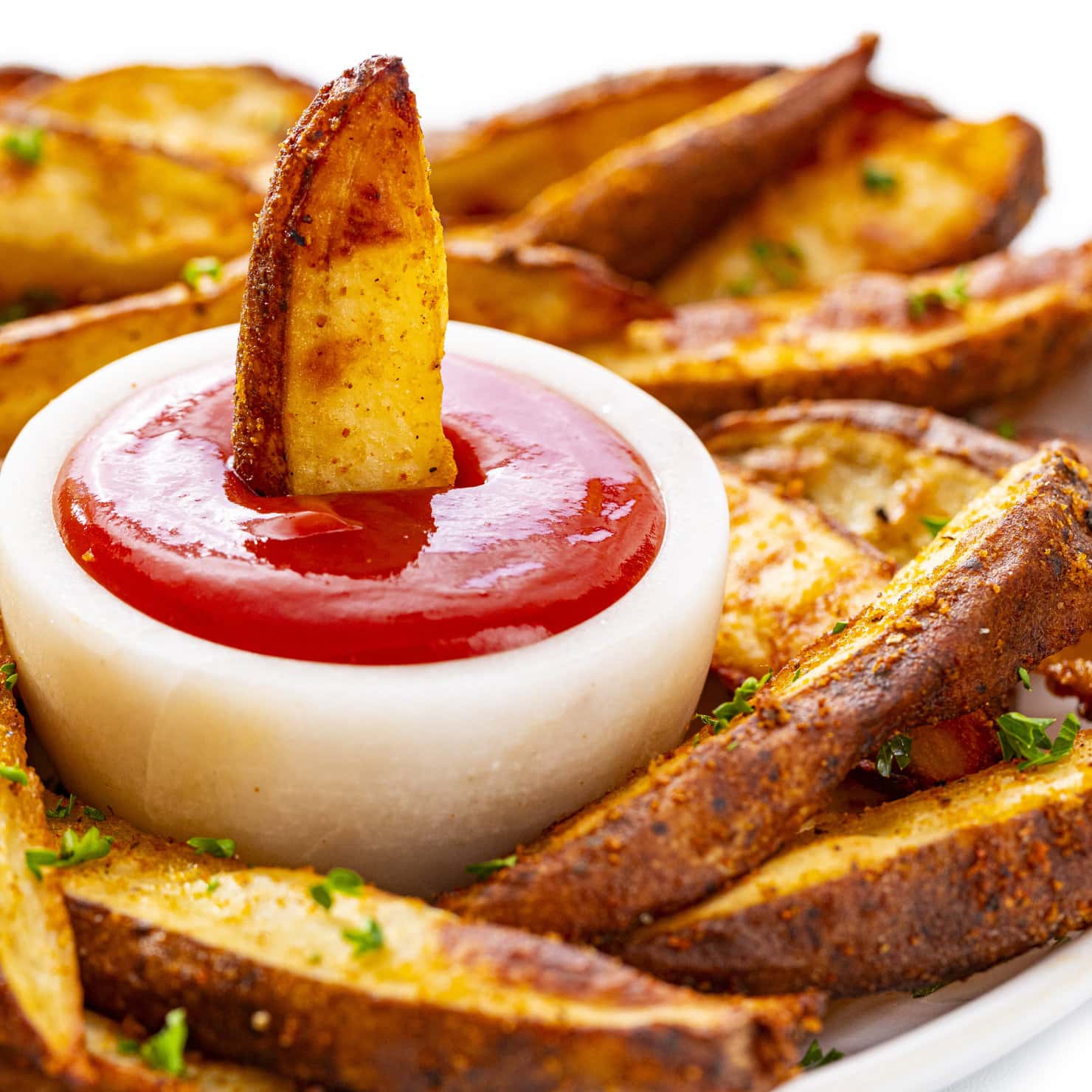 Steak fries on a plate with one dunked in ketchup.