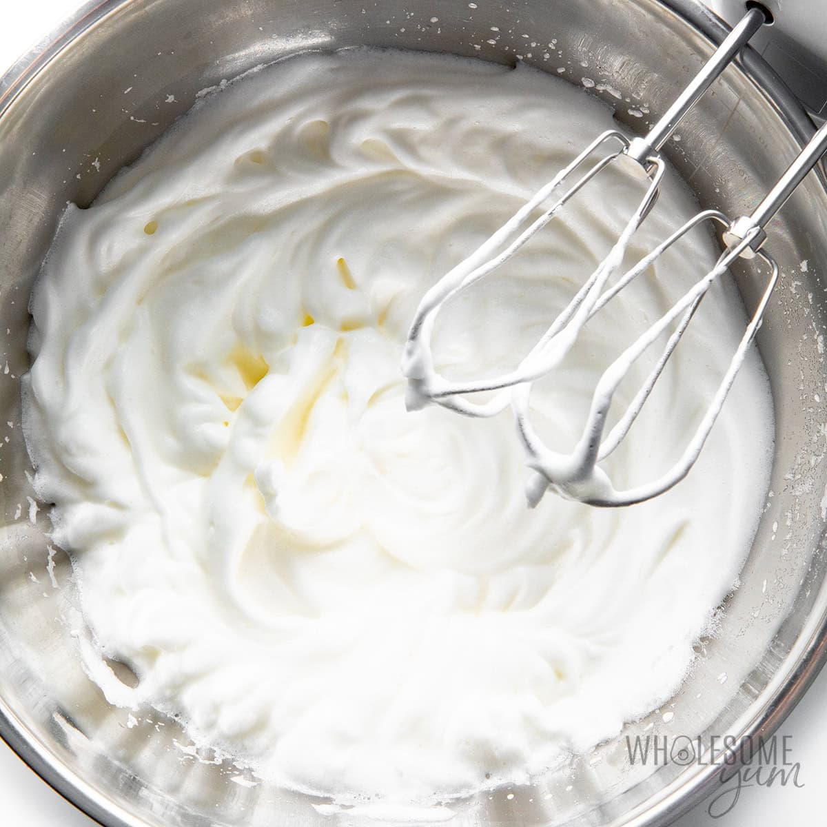 Whipped egg whites in a bowl with hand mixer.