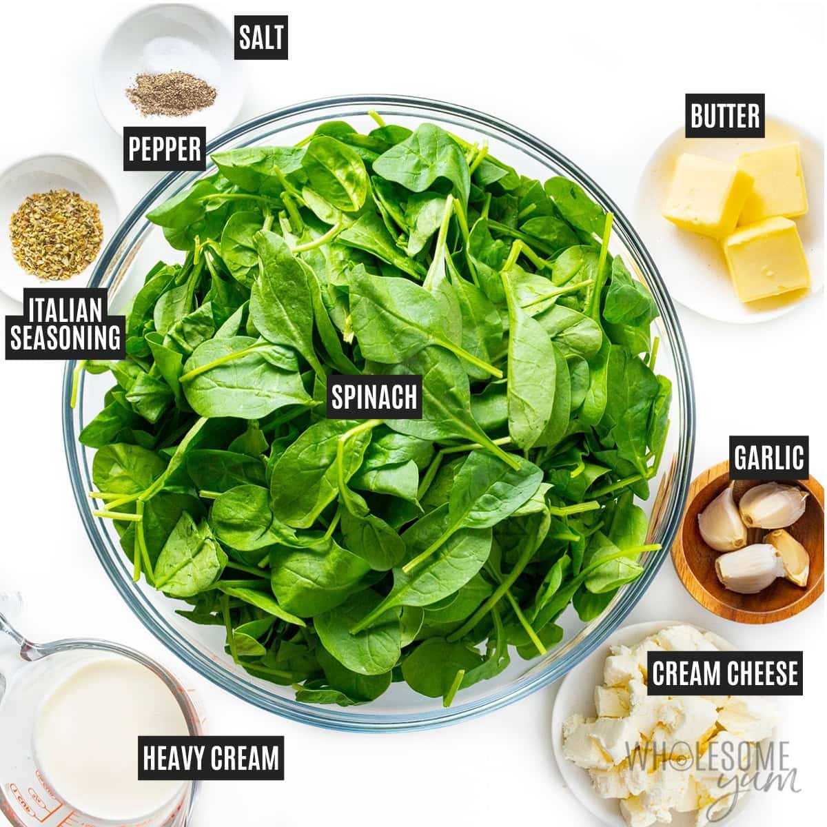 Bowl of spinach next to cream, butter, garlic, cream cheese, and spices.