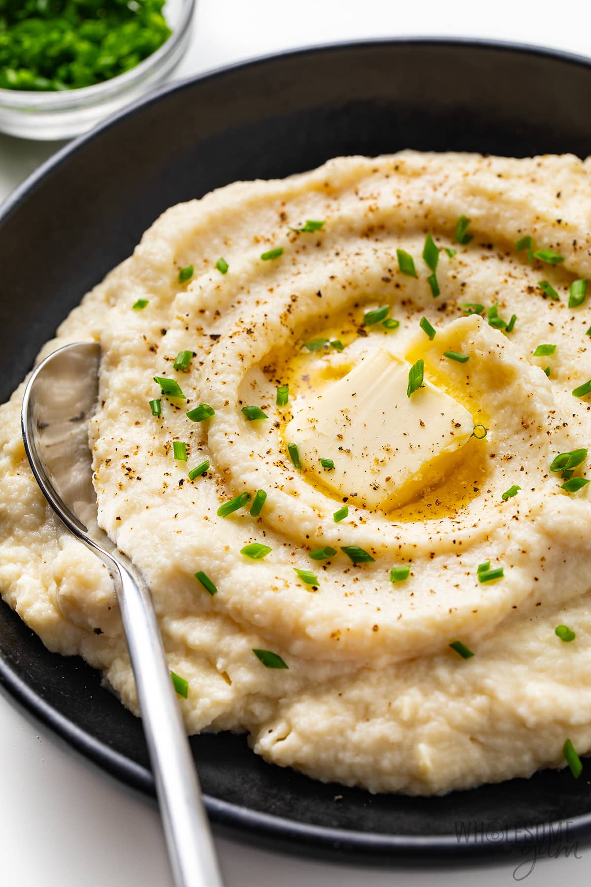 Cauliflower mashed potatoes in a bowl with butter, chives, and a spoon.