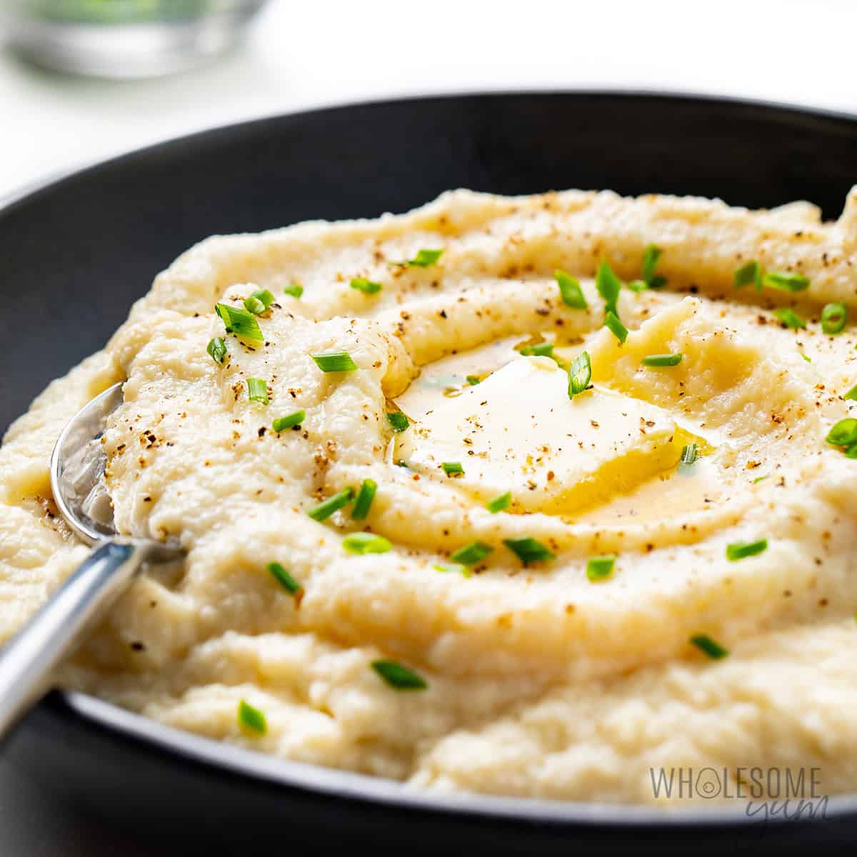 Mashed cauliflower recipe in a bowl and topped with butter and chives.
