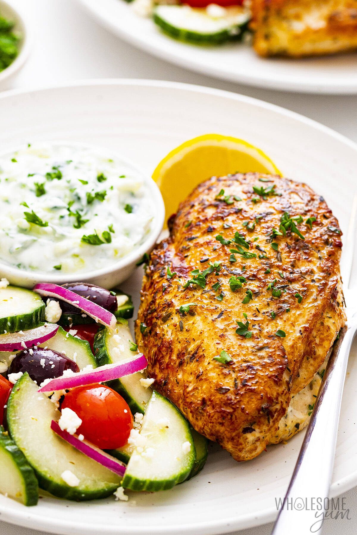 Yogurt marinated chicken on a plate with Greek salad with tzatziki sauce.