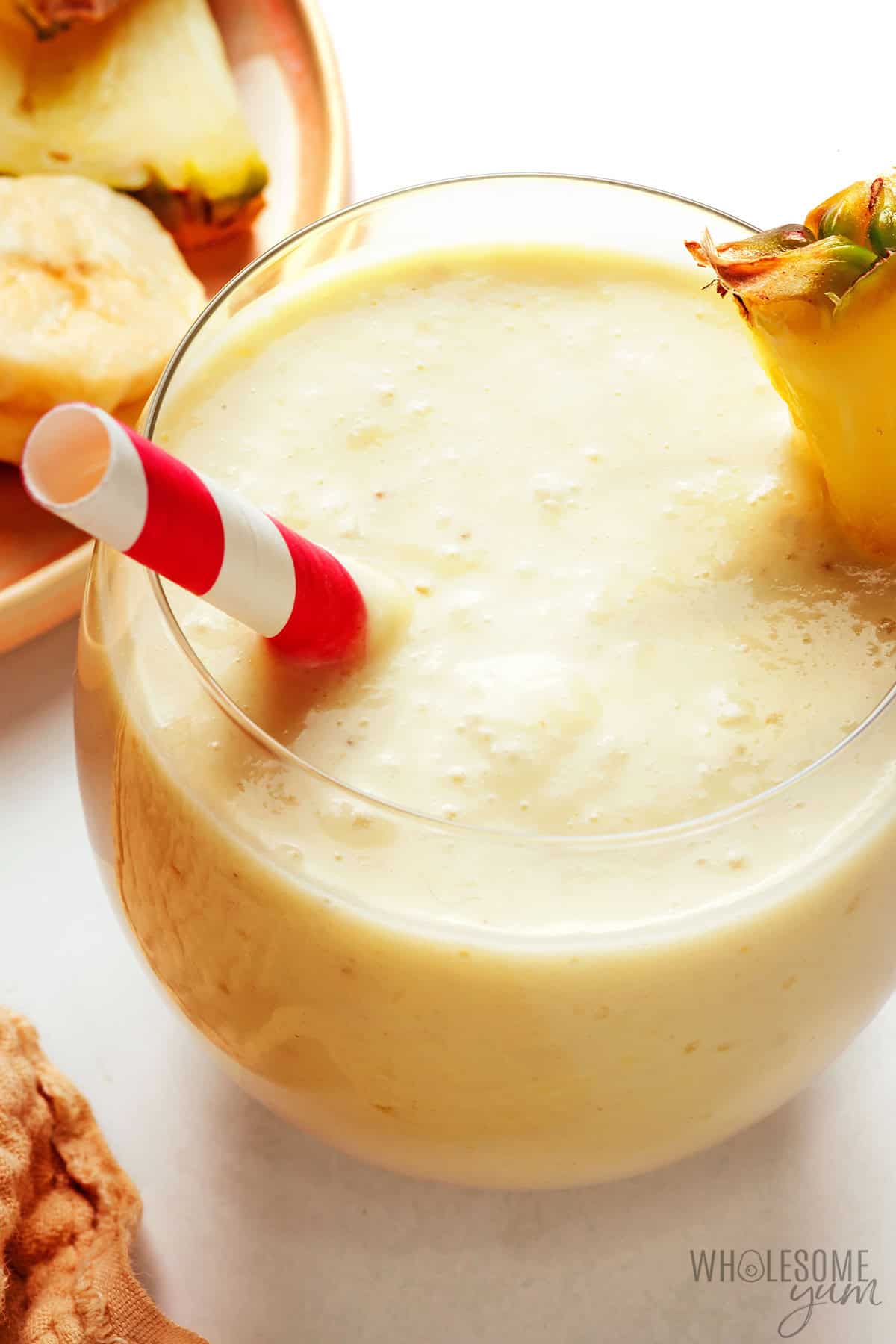 Thick, creamy tropical pineapple smoothie with a wedge of pineapple and a straw.
