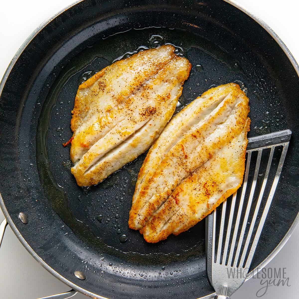 Searing barramundi fillets in a skillet.