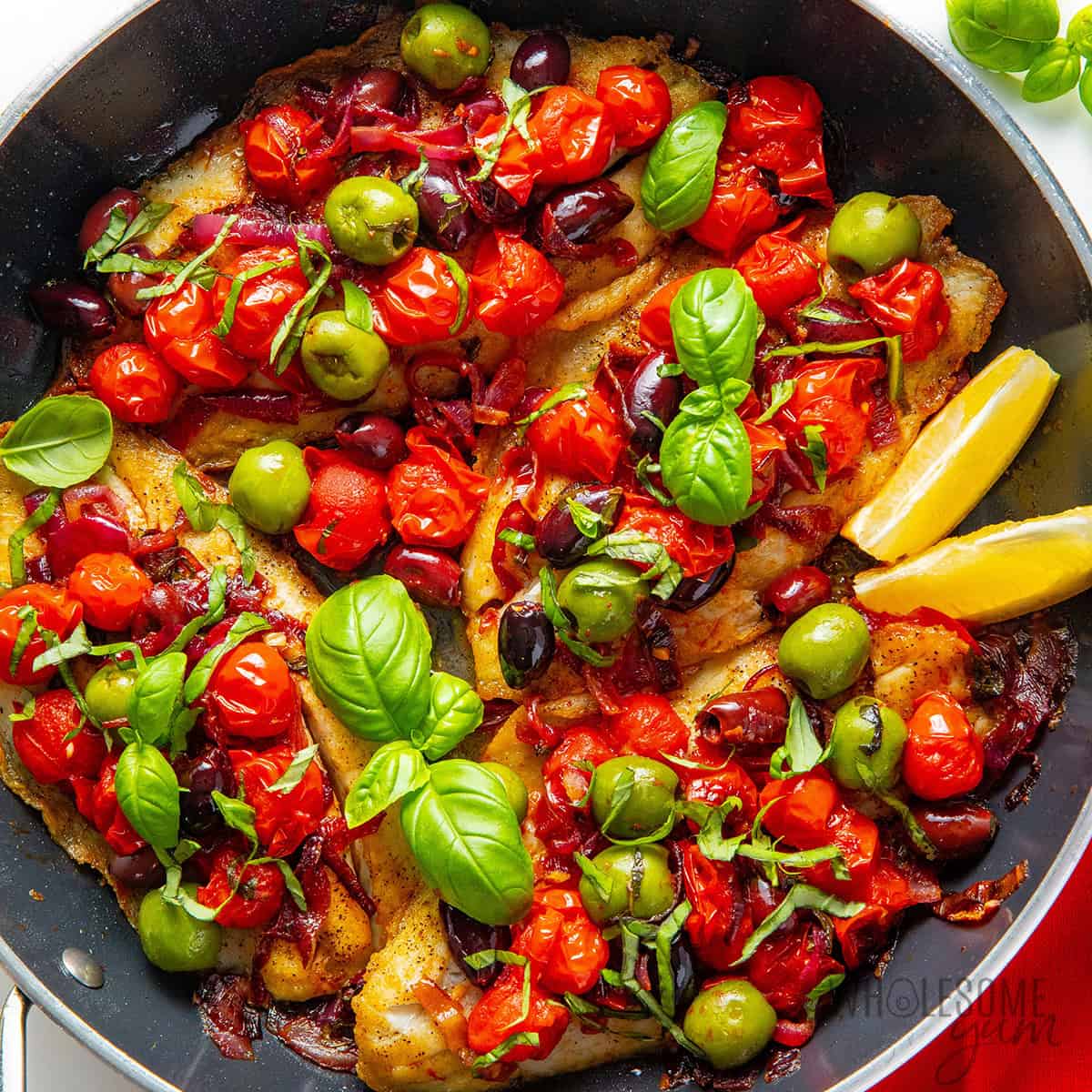 Finished barramundi recipe topped with tomatoes, olives, and fresh basil.