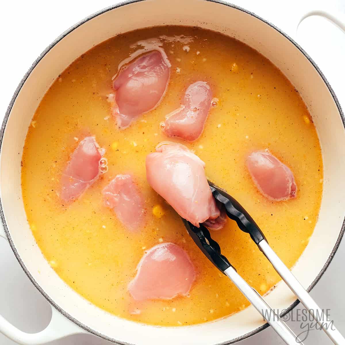 Blended corn, green chilies, broth, salt, pepper, and chicken thighs added to the pot.