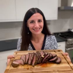 Maya holding a cutting board with sliced medium rare flat iron steak.