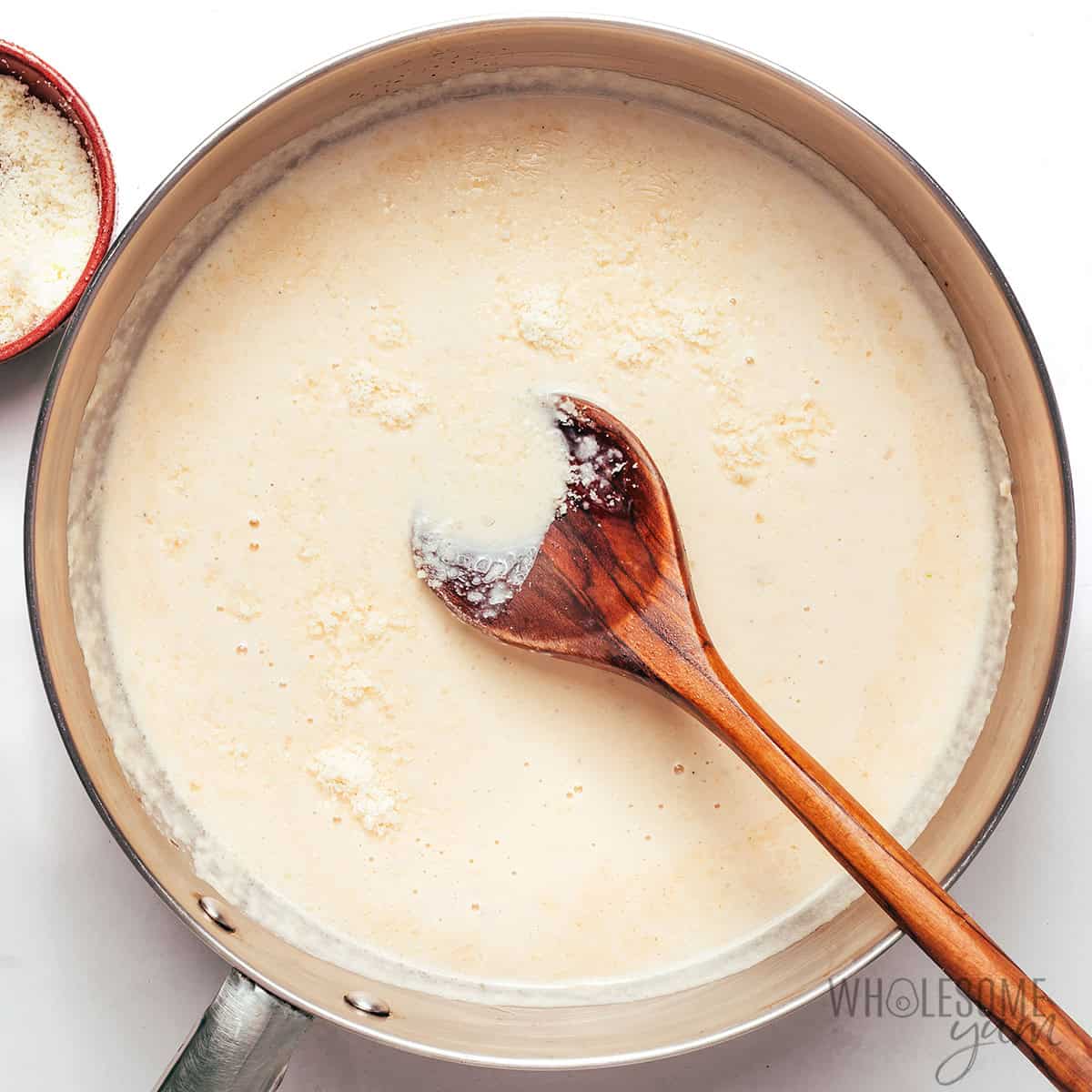 Stirring grated parmesan into the creamy sauce base.