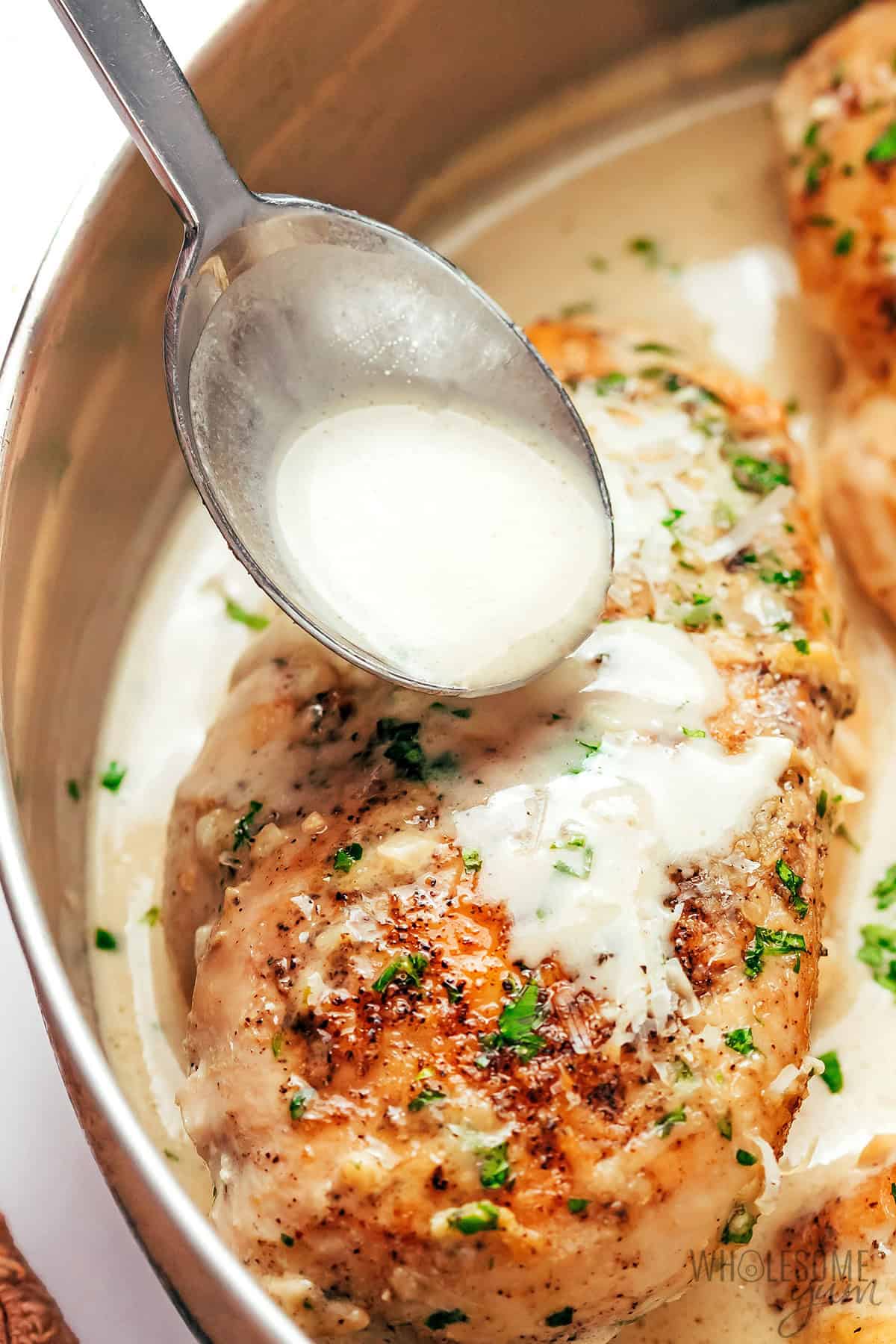 Creamy garlic parmesan chicken with sauce drizzled on it from a spoon.