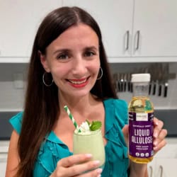 Maya holding a minty healthy shamrock shake and a bottle of liquid allulose.