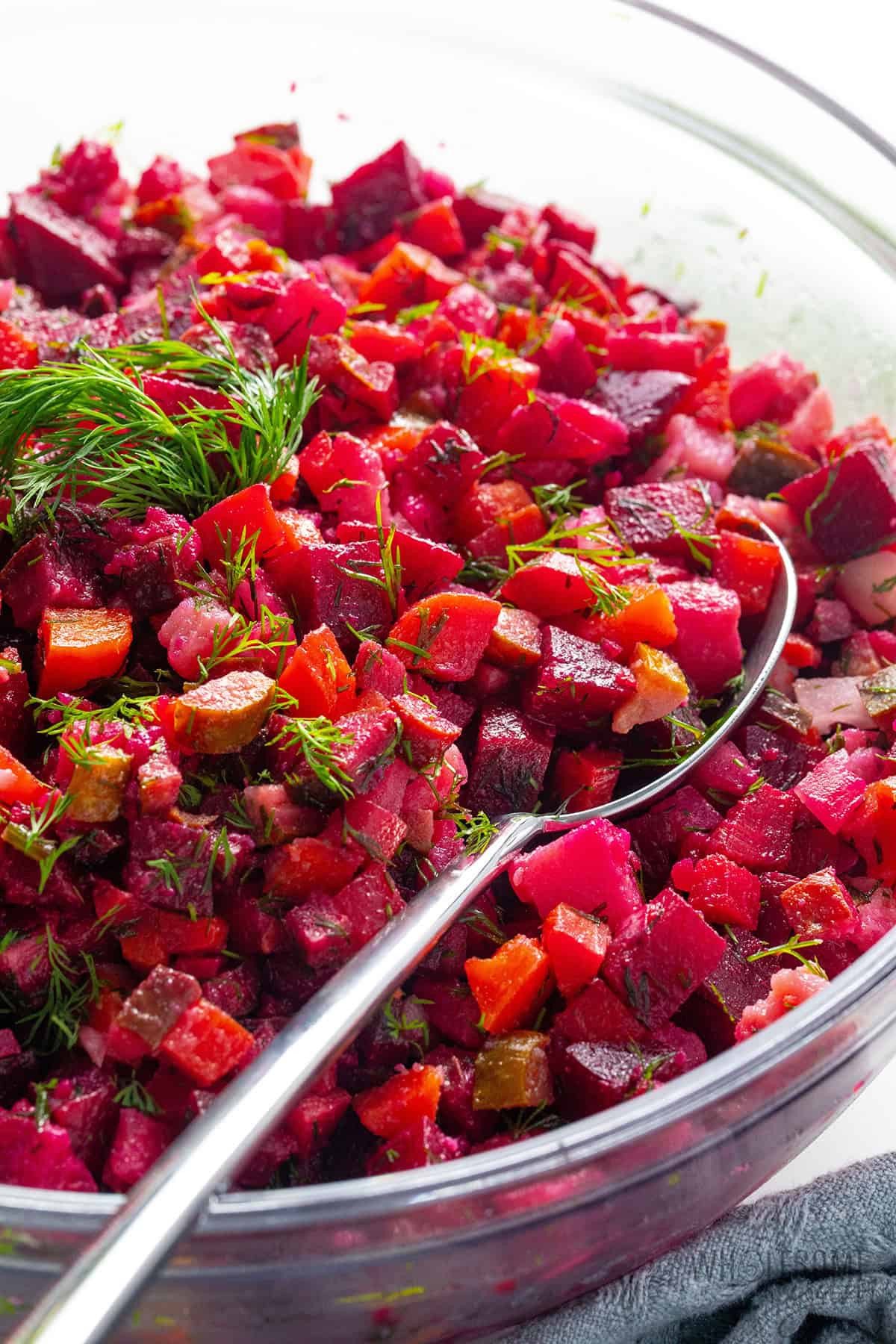 Vibrant Russian salad in a bowl with fresh dill and a spoon for serving.