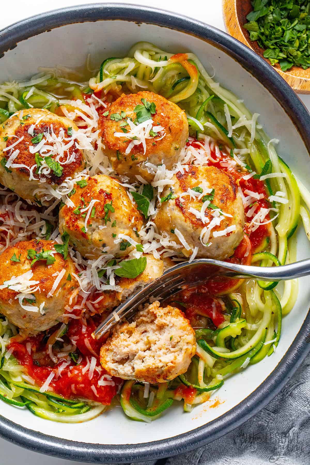 Juicy ground turkey meatballs in a bowl with zoodles and sauce, and one cut open to show the juicy texture inside.
