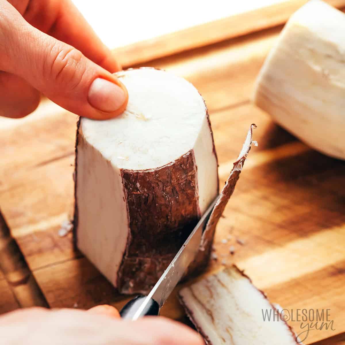 Peeling the skin off an upright yuca with a knife.
