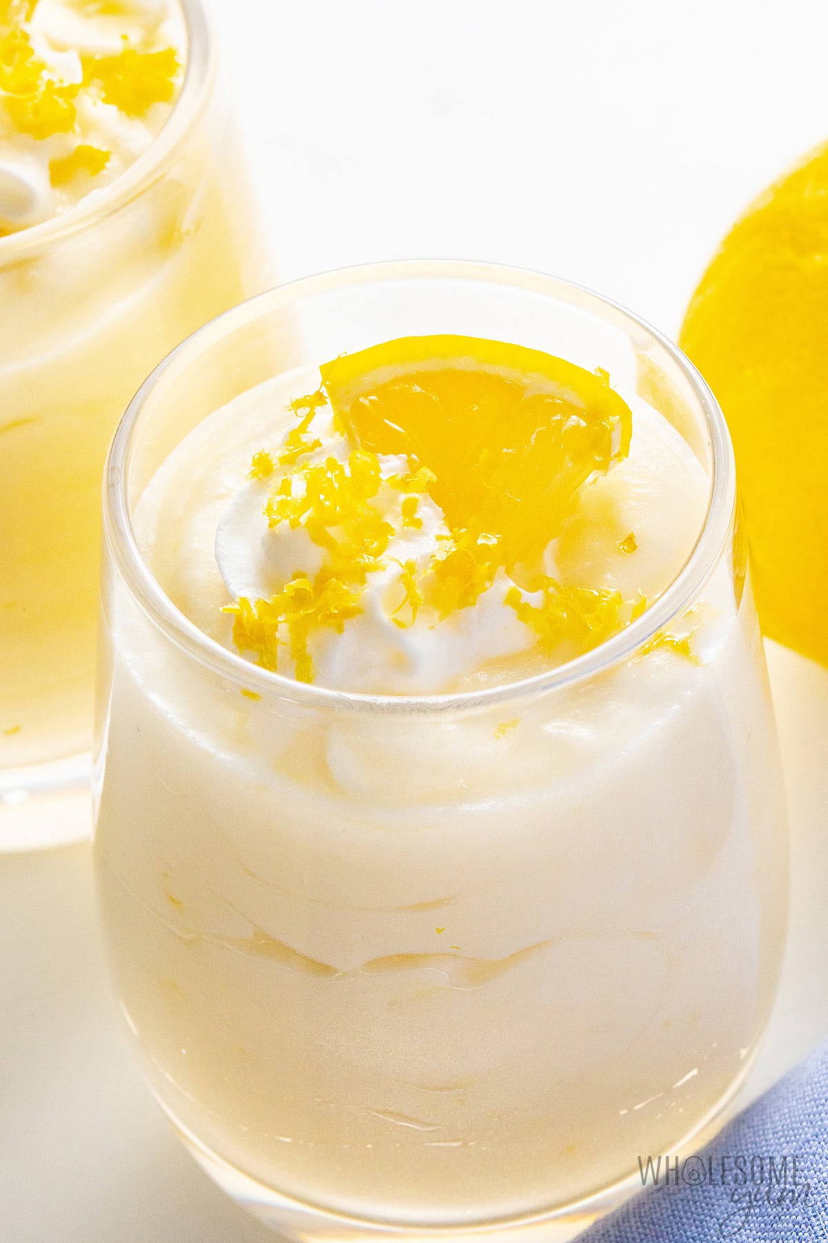 Creamy lemon mousse in a cup with whipped cream, lemon zest, and lemon slice.