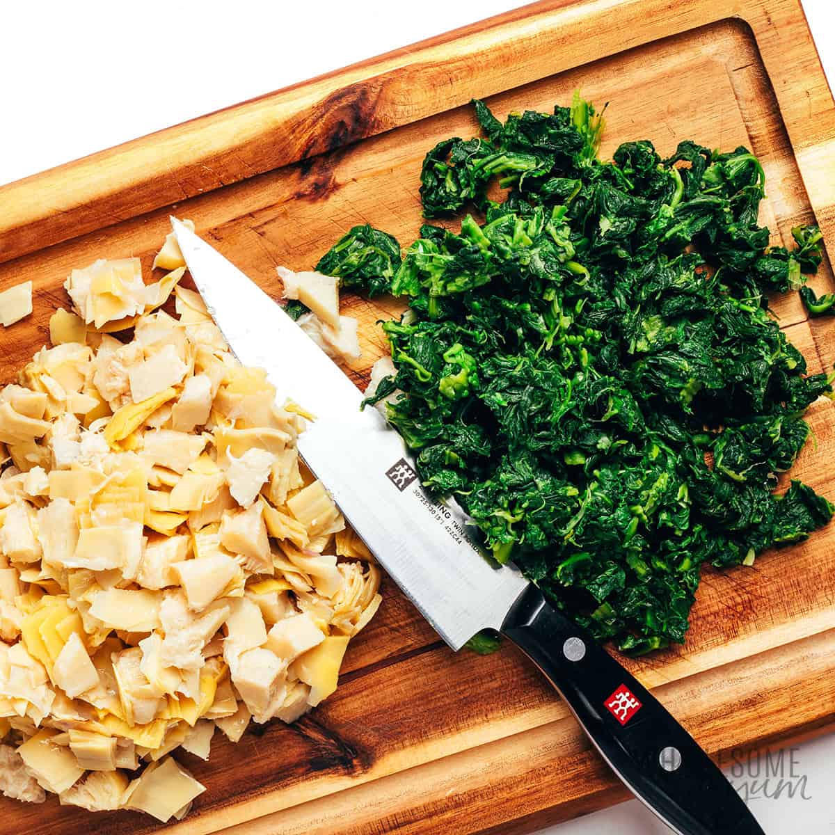 Drained spinach and artichokes chopped on a cutting board.