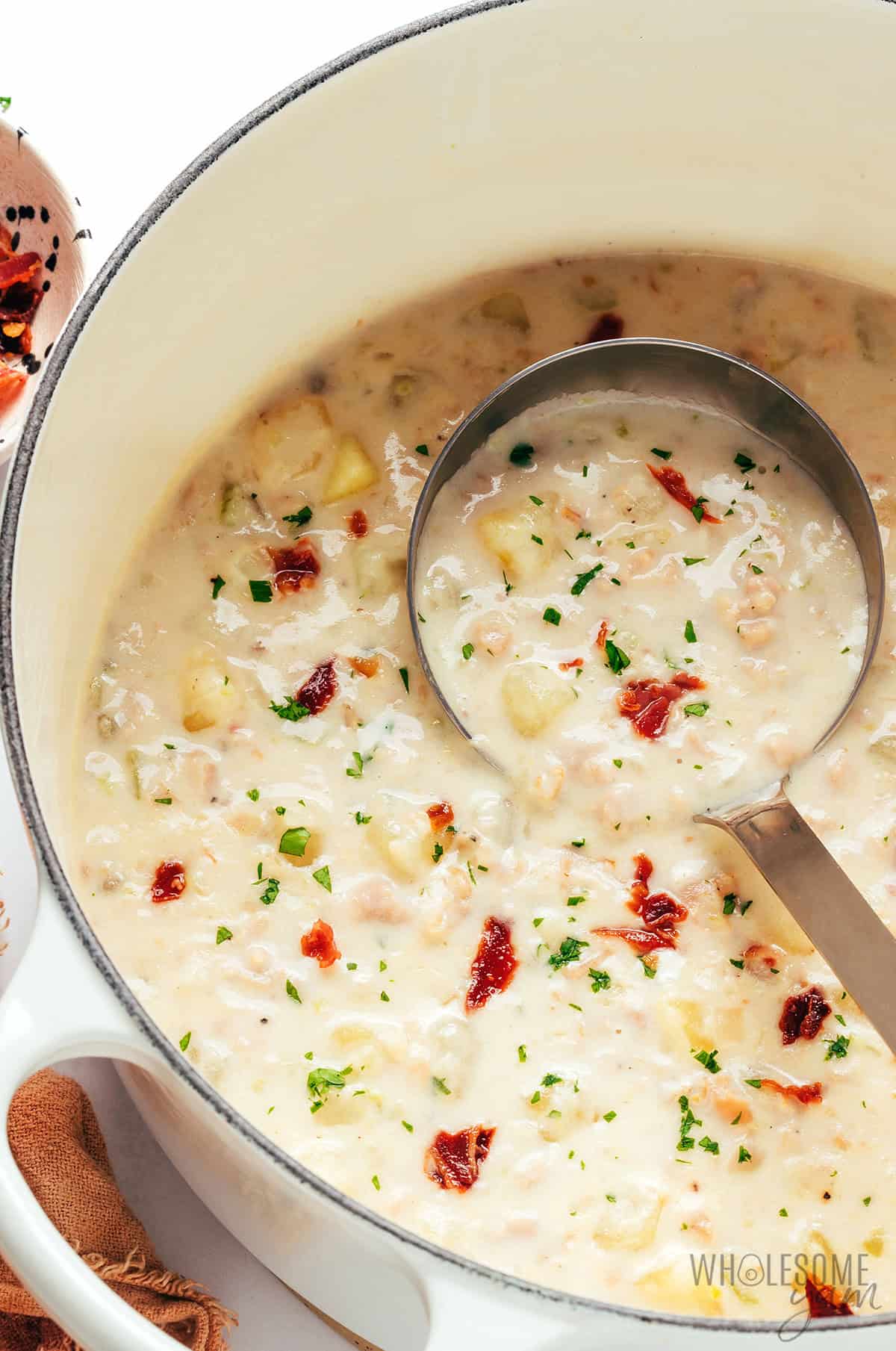Thick, creamy clam chowder in a Dutch oven with a ladle.