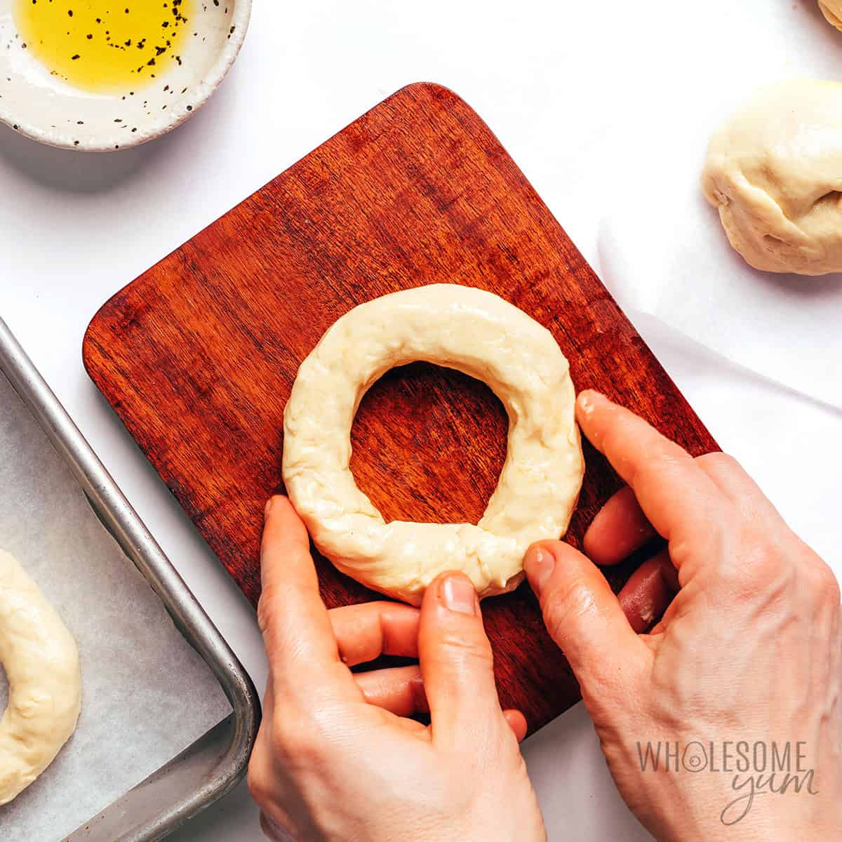 Shaping cottage cheese bagel dough into rings on a parchment lined baking sheet