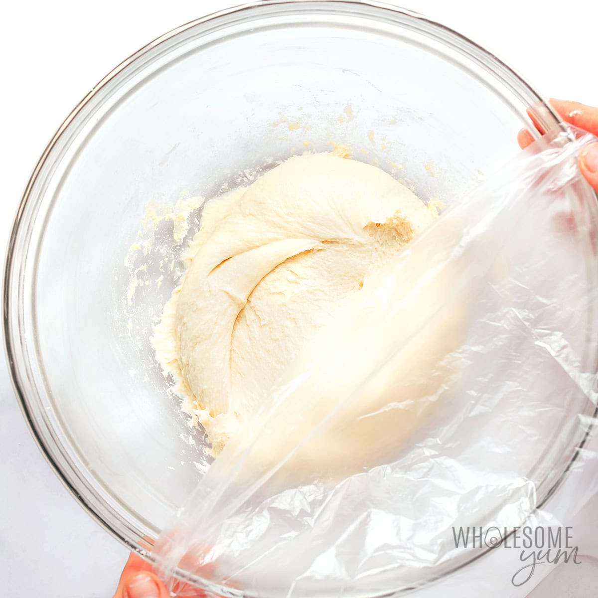 Covering dough with plastic wrap to chill in the fridge.