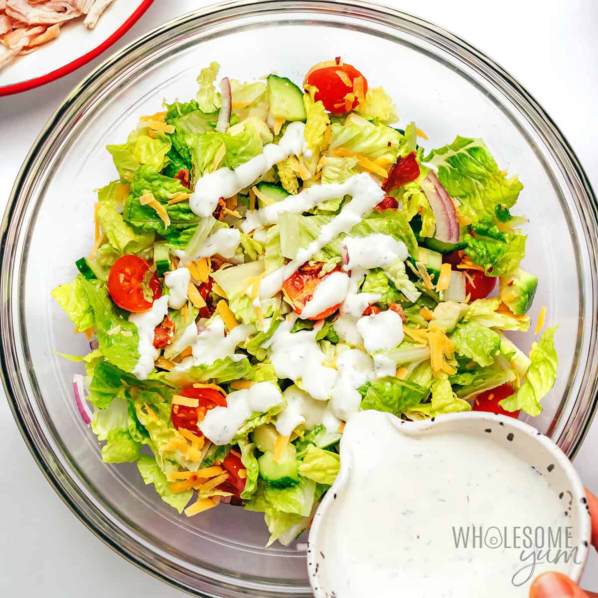 Drizzling ranch dressing over the salad.