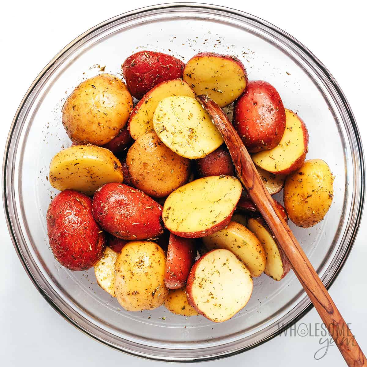 Seasoned potato halves in a bowl with a spoon.