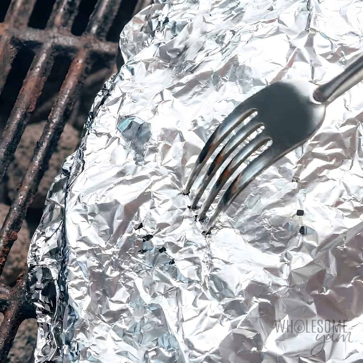 Testing the grilled potatoes in foil with a fork.