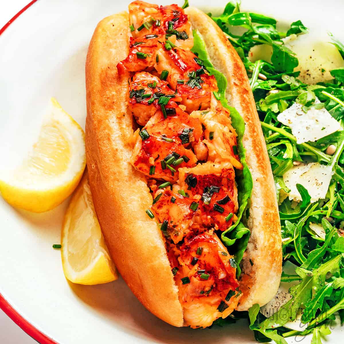 Finished lobster roll recipe served with arugula salad and lemon wedges.