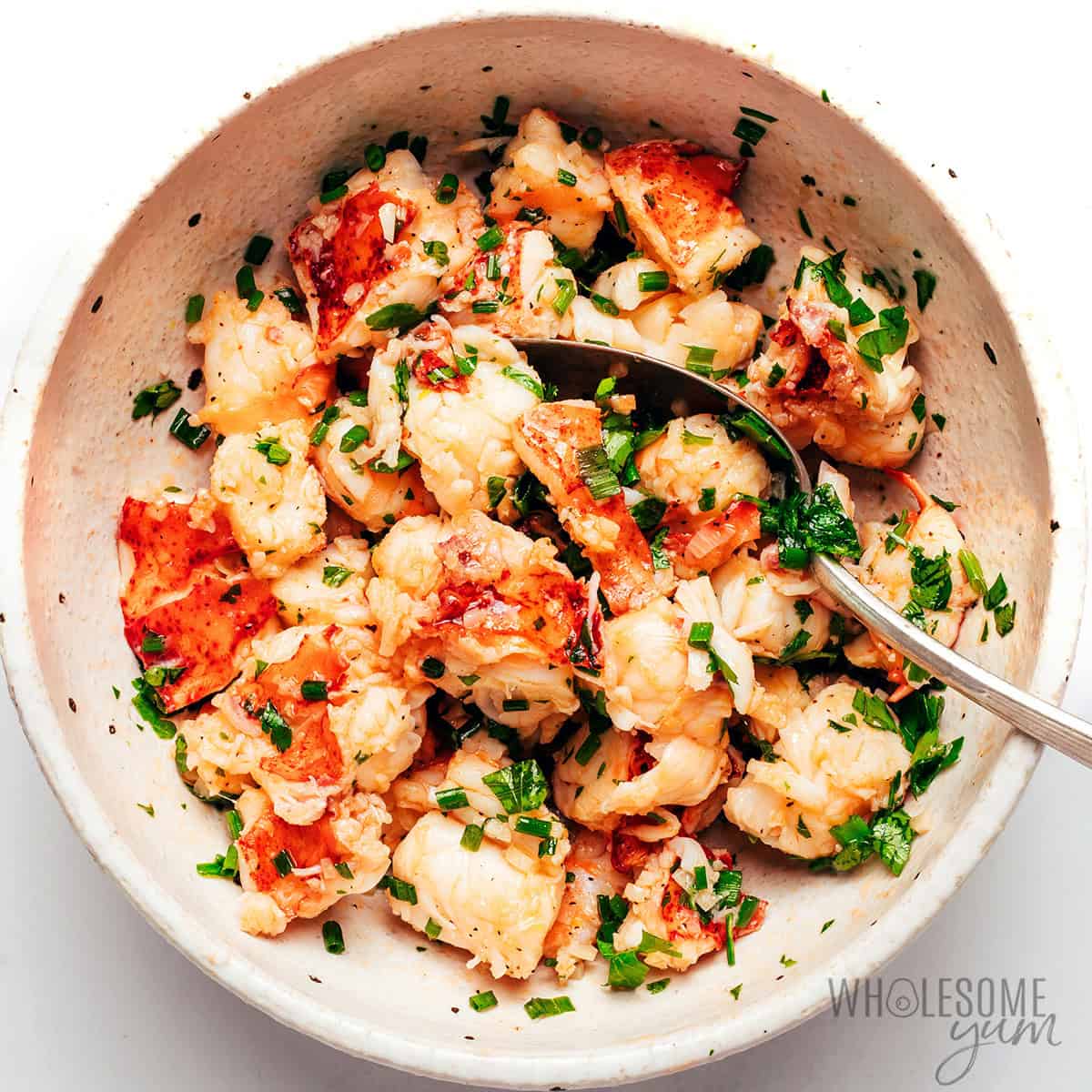 Buttery lobster chunks tossed with fresh herbs in a bowl.