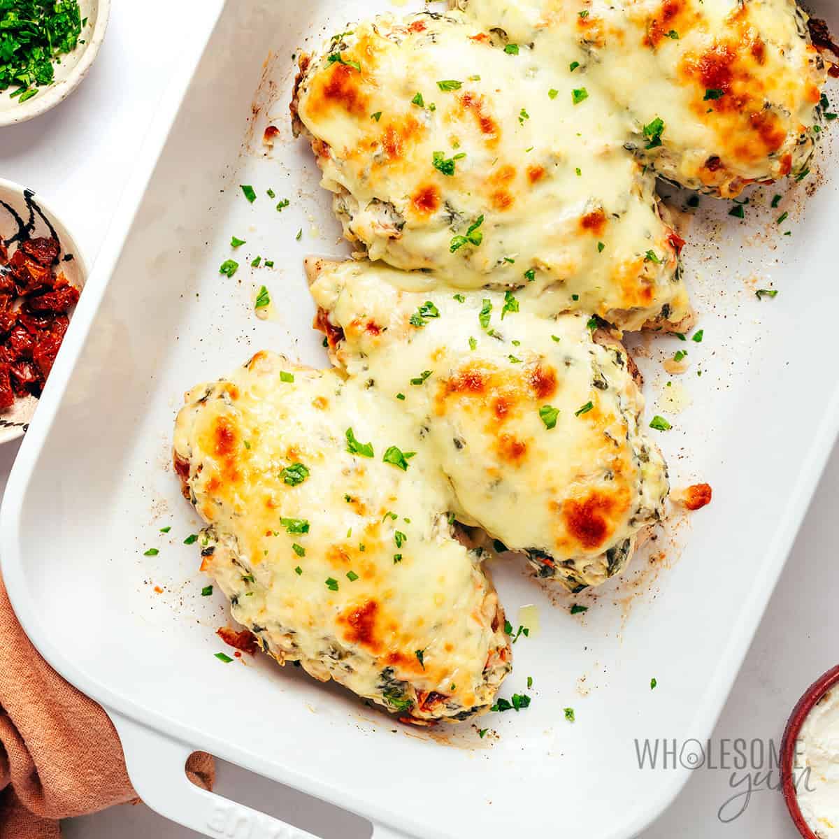 Baked spinach artichoke chicken with golden brown cheese and parsley garnish.