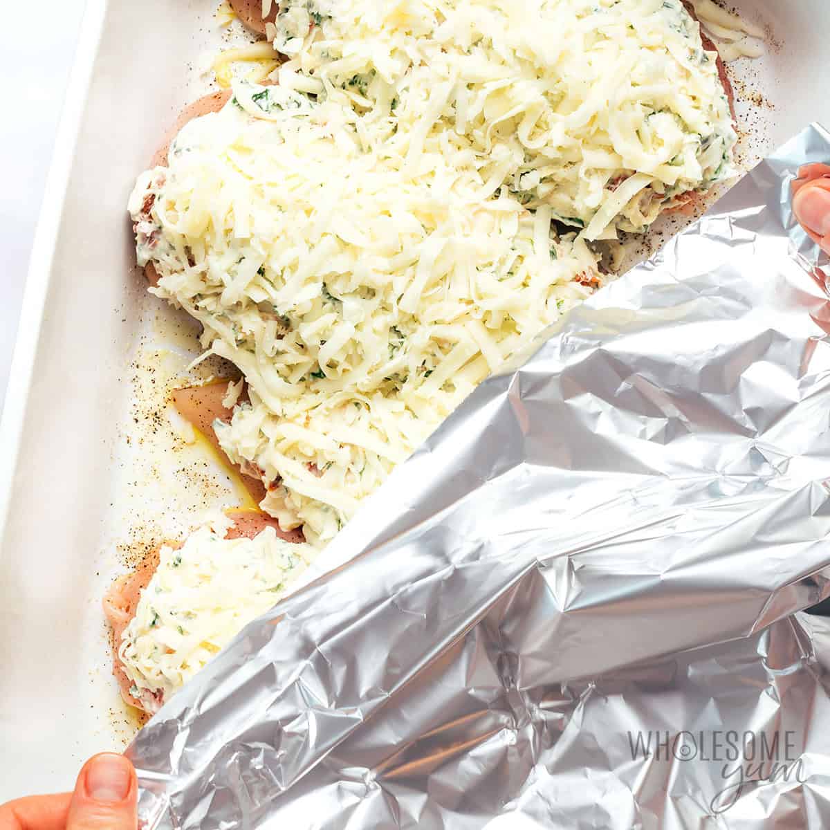 Cheese added over the spinach artichoke chicken and covering it in foil.