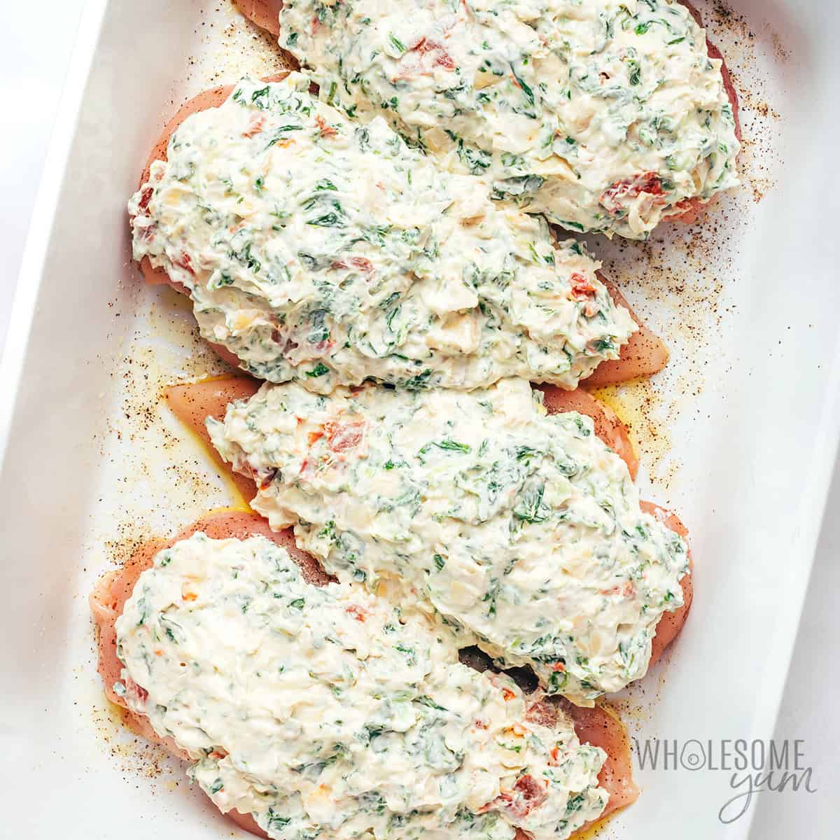 Spreading spinach artichoke mixture on top of chicken.