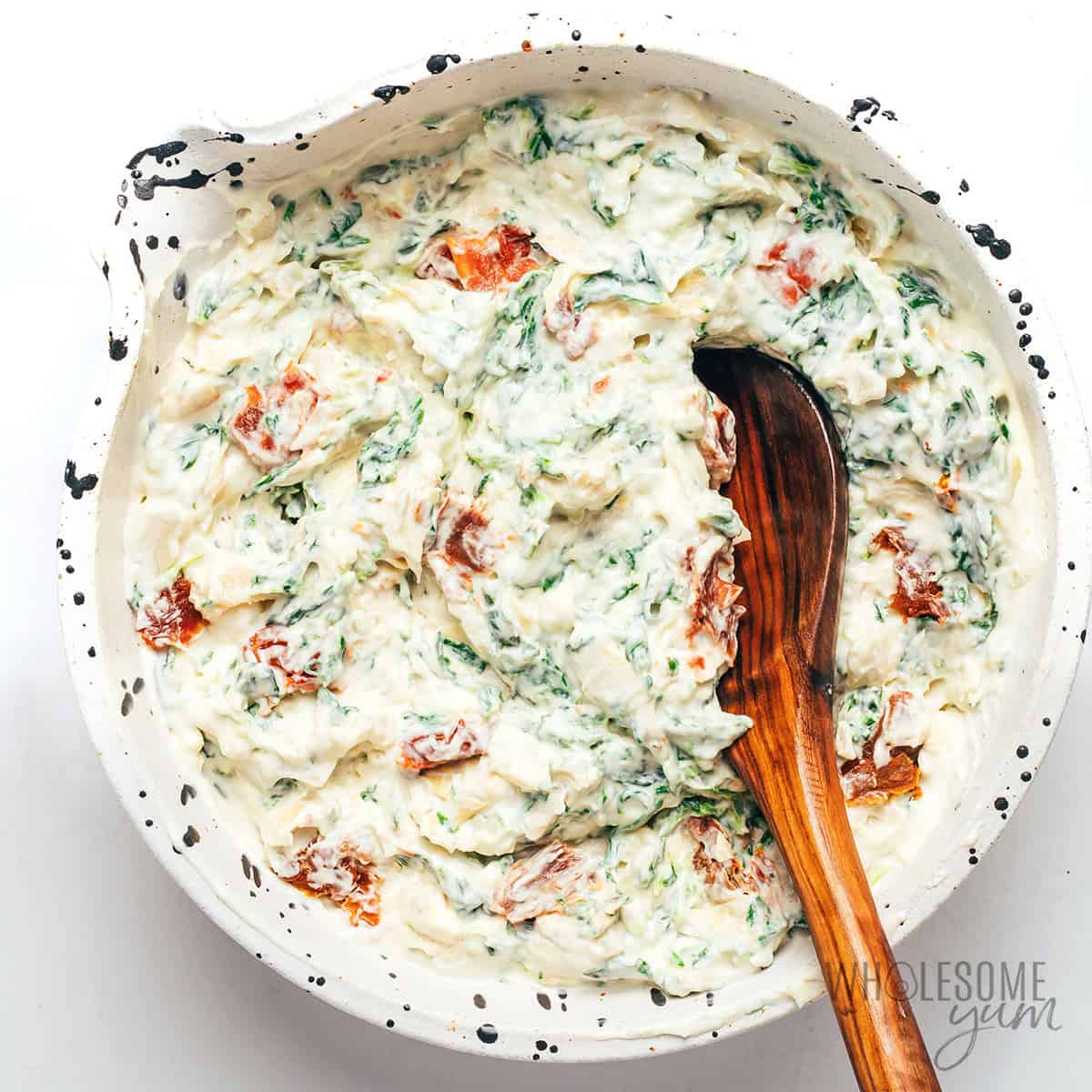 Creamy spinach artichoke dip base in the bowl, with sun-dried tomatoes and garlic added.