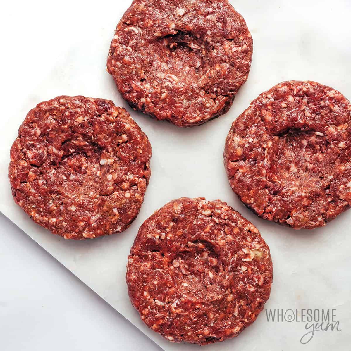 Bison burger patties on a cutting board with thumbprints.