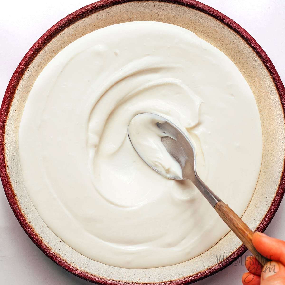 Spreading the creamy bruschetta dip base in a shallow bowl.